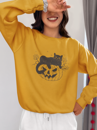 Wearing the Pumpkin Cat Sweatshirt—a yellow Halloween-themed garment perfect for cat lovers featuring a black cat sitting on a carved pumpkin—a woman playfully smiles while covering one eye with her hand, completing the spooky season look with white pants.